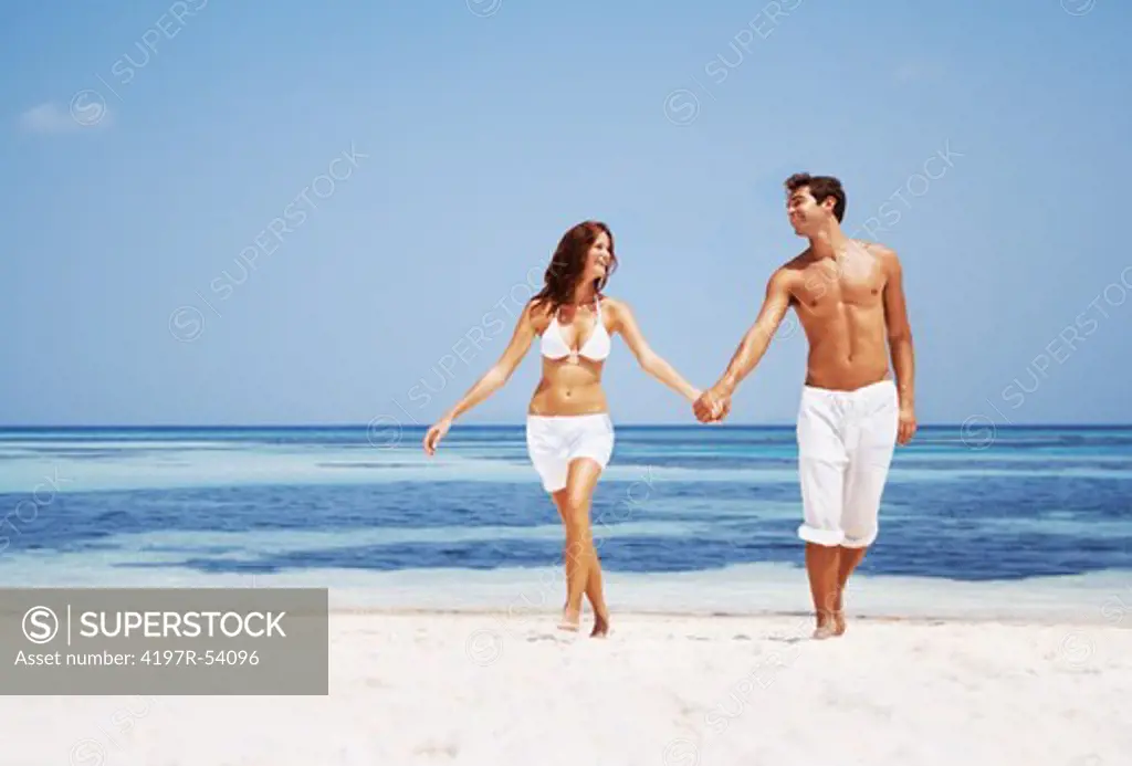 Portrait of attractive young couple walking on the beach holding hands