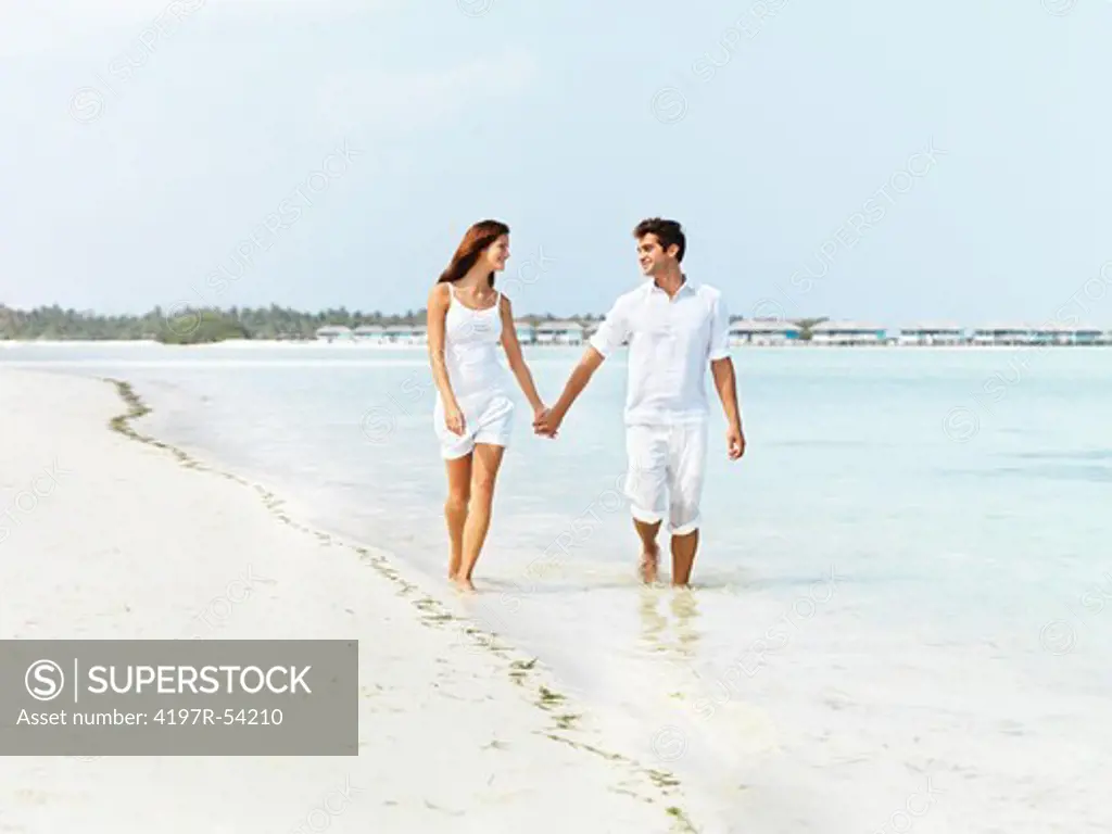 Happy young couple walking along the seashore and holding hands