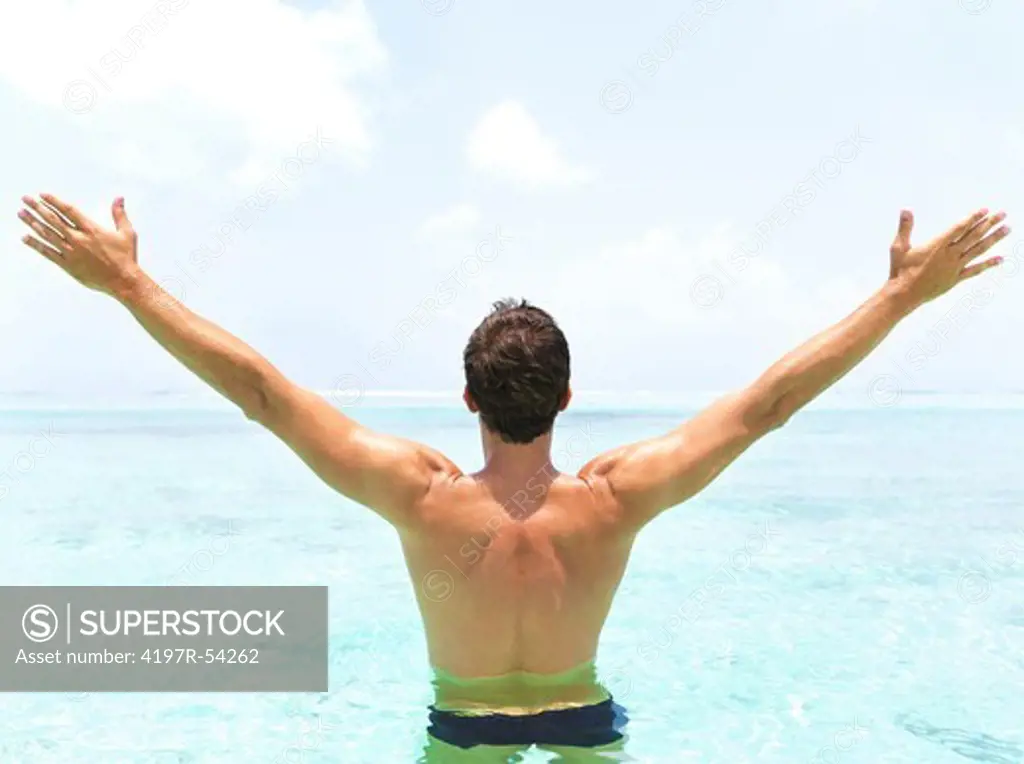 Rear view of a man in the ocean raising his palms to the horizon