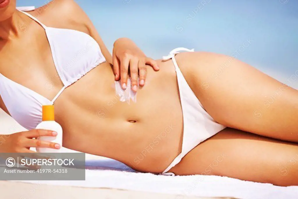 Portrait of woman applying sunscreen lotion on her stomach at beach