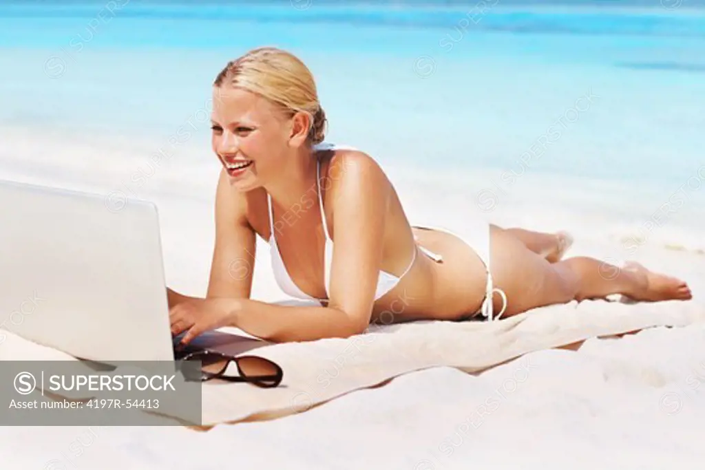 Full length of happy young woman surfing internet while relaxing on beach