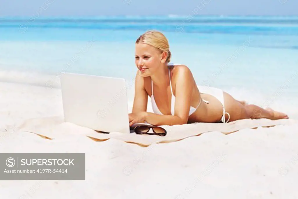 Full length of young woman in bikini with laptop relaxing at beach