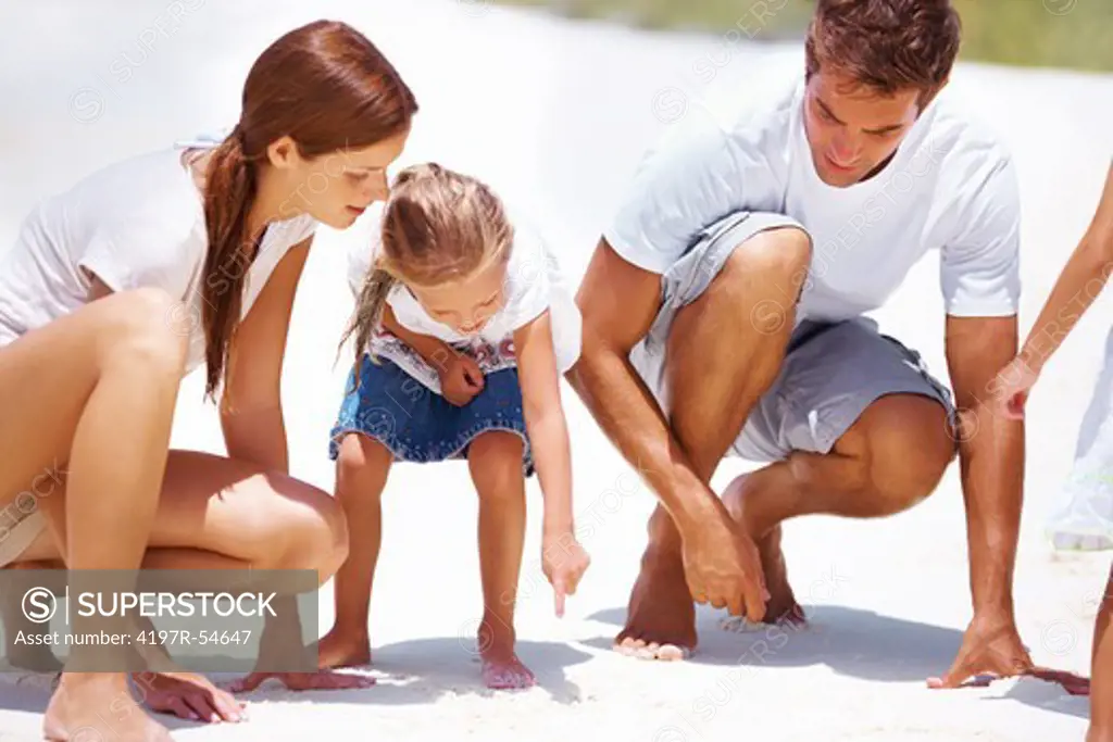 Cute little girl pointing at something on the sand and showing her parents