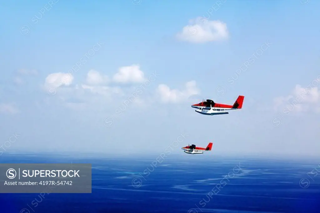 Two seaplanes flying overhead with the blue ocean horizon as their background