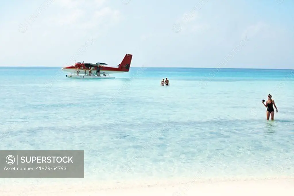 Docked seaplane out in the shallow waters as its passengers wade the waters towards the beach