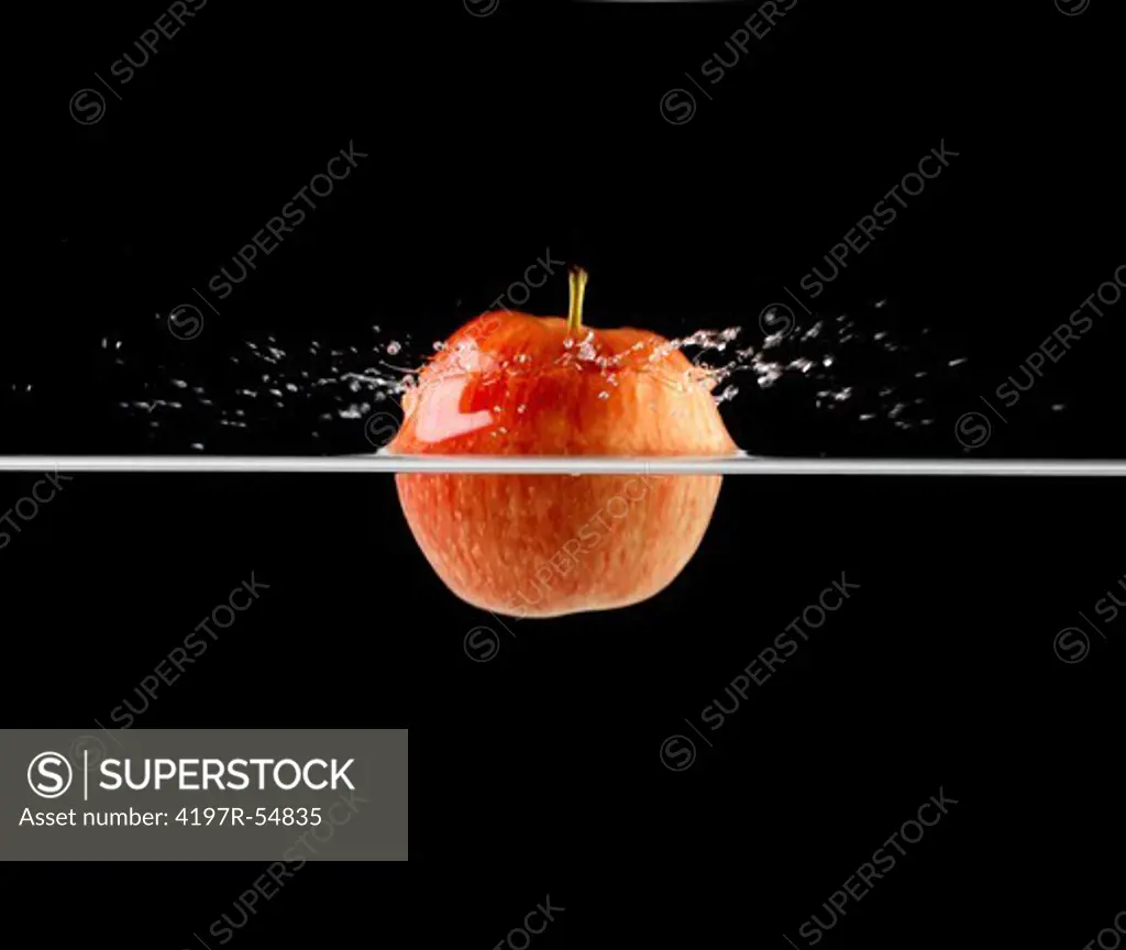 Red apple breaking the waters surface as it is dropped - Isolated on black