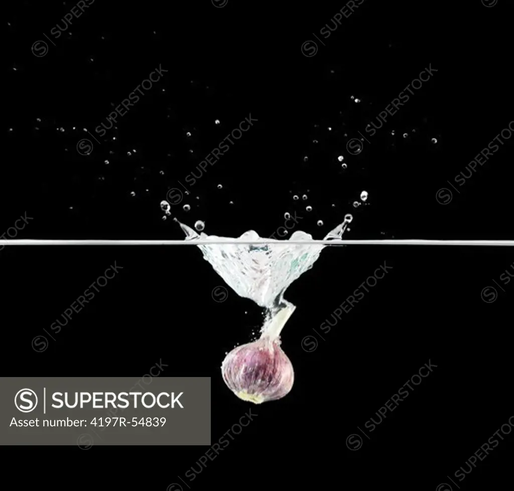 Purple onion dropping into water while isolated on black