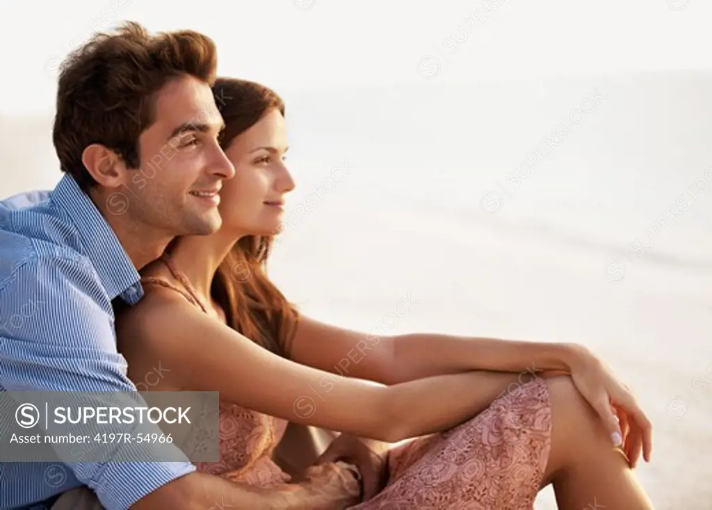 Portrait of affectionate young couple sitting on the beach and enjoying life