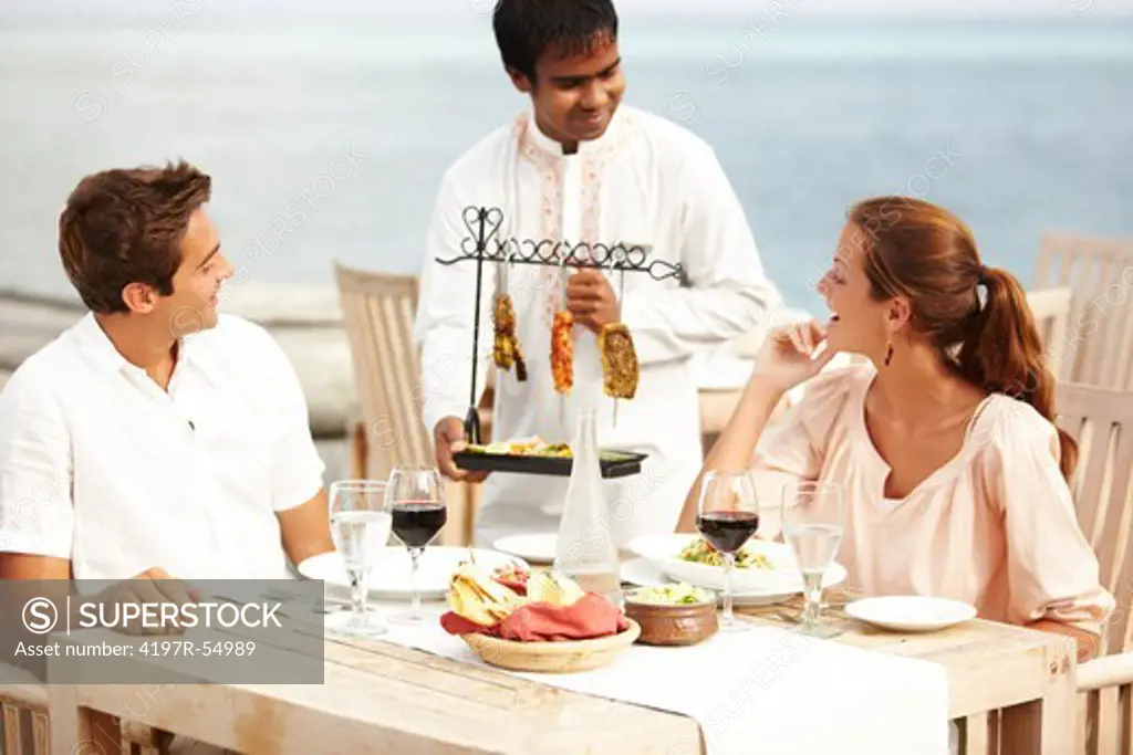 A waiter presents a couple with their main course - a selection of meats on a rack