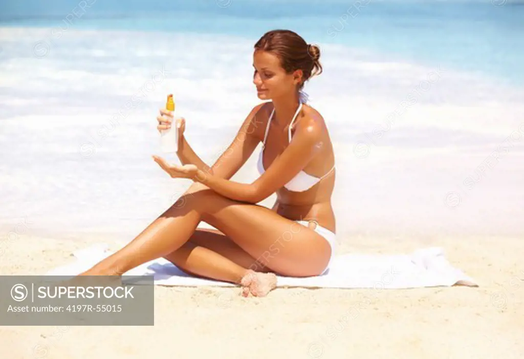 Portrait of beautiful woman applying suntan lotion at beach