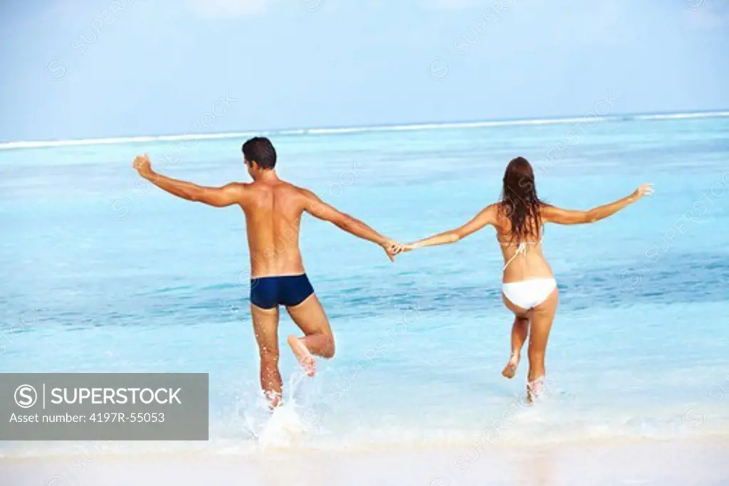 Rear view of woman walking with man on beach while holding hands