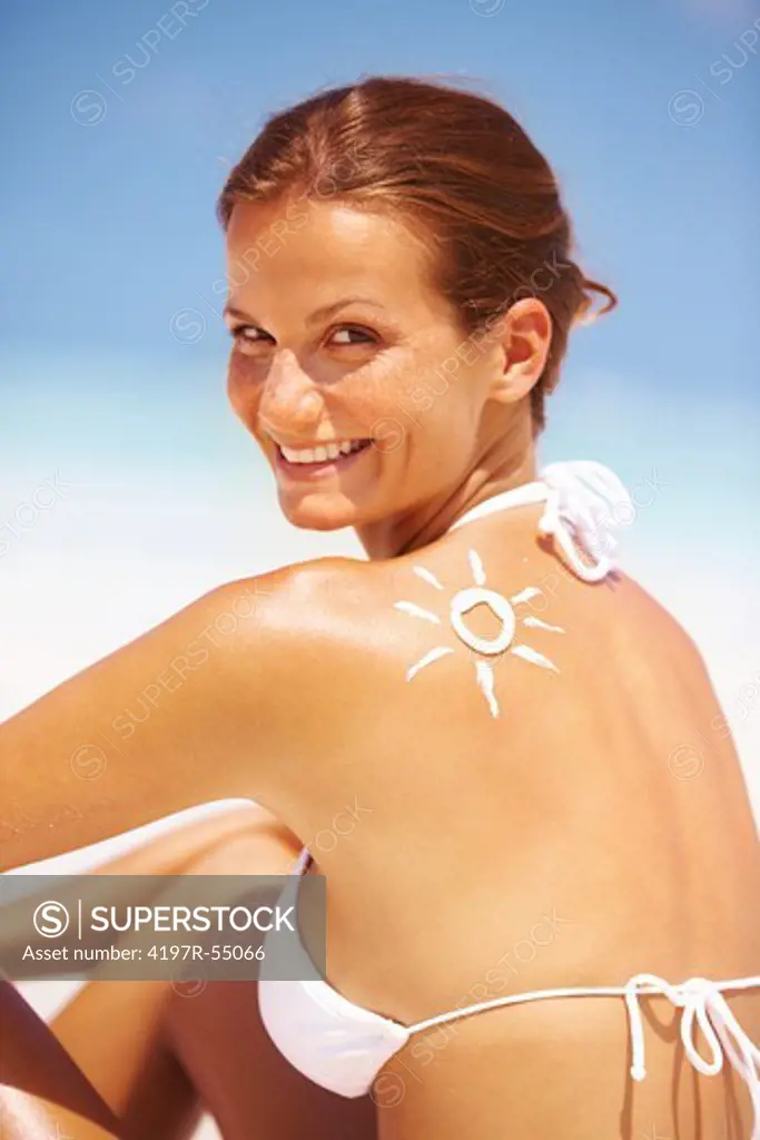 Portrait of beautiful young woman smiling with drawn sun on shoulder at beach
