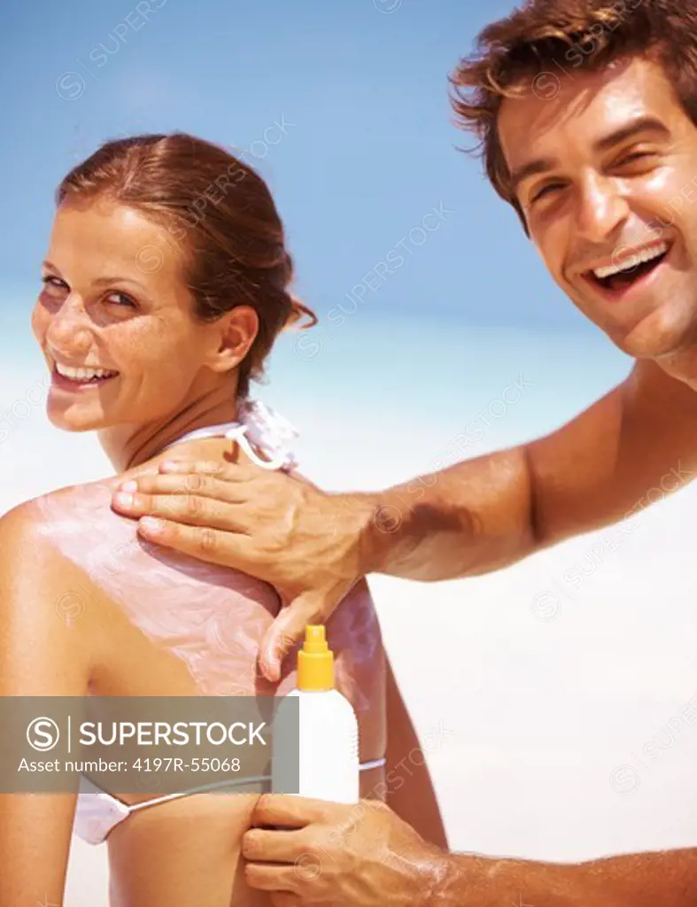 Portrait of happy young couple applying sun block lotion for preventing sunburn