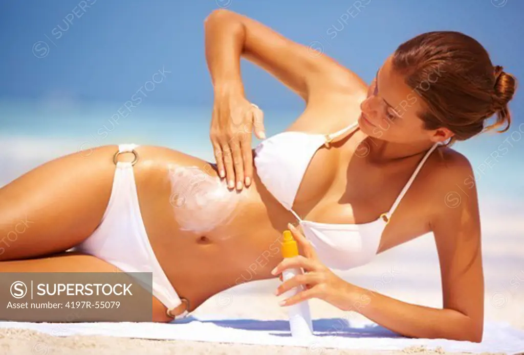 Portrait of beautiful young woman applying suntan lotion on stomach at beach