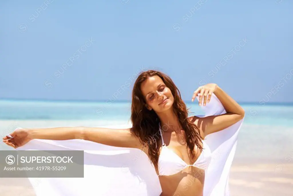 Portrait of beautiful young woman enjoying breeze at beach with sarong