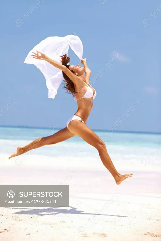 Portrait of carefree young woman in bikini jumping at beach