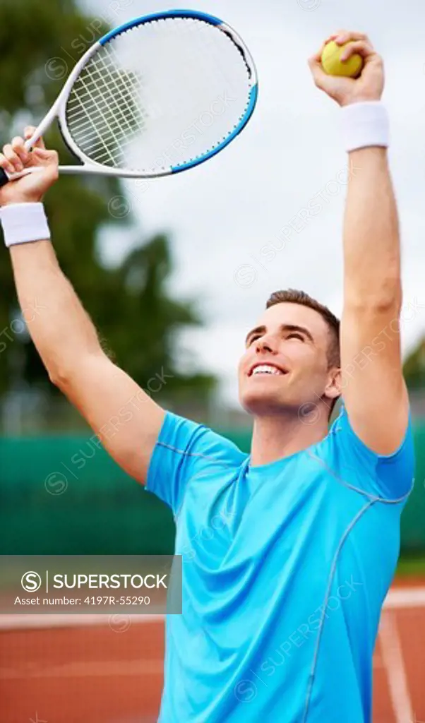 Handsome young tennis player expressing triumph by holding up his racquet and tennis ball