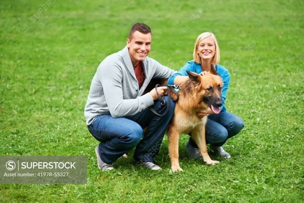 Happy young couple sitting in a park with their German Sheperd and smiling at the camera