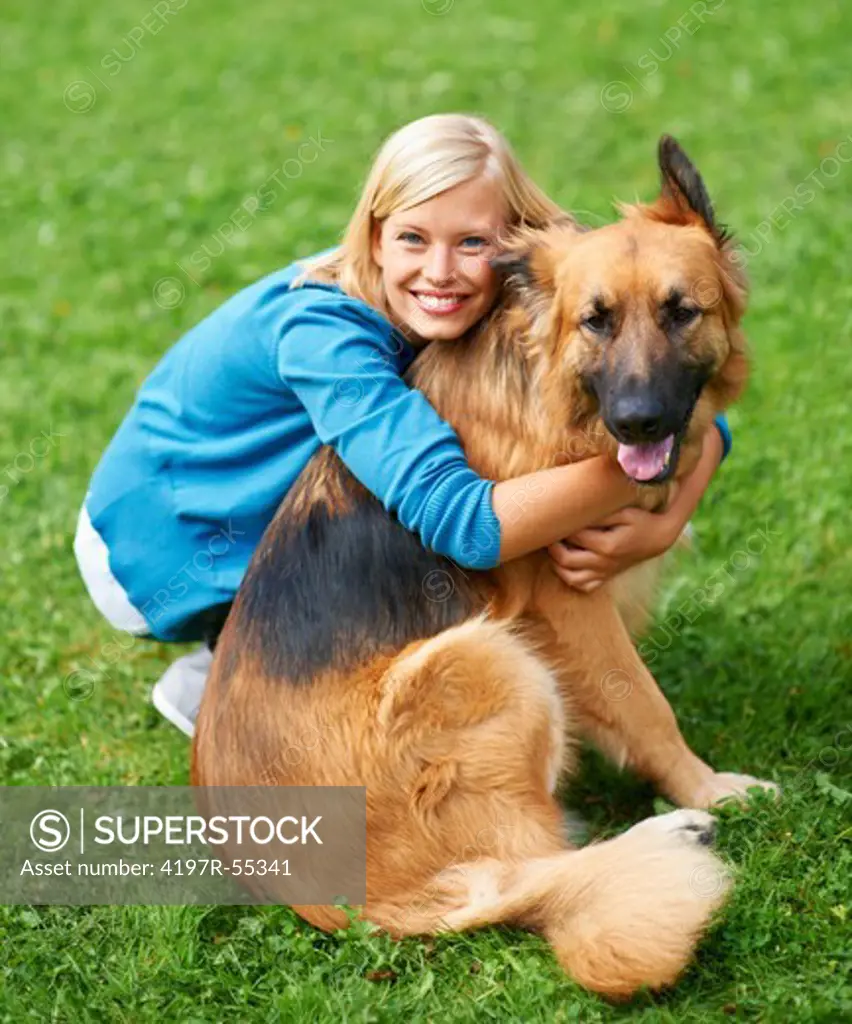 Lovely young blonde woman hugging her German Sheperd and looking at the camera