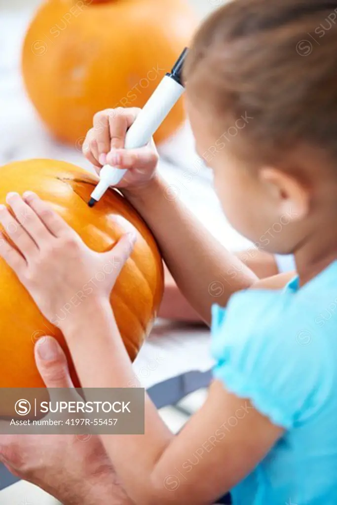 Rear view of a little girl drawing the eyes onto a jack-o-lantern for Halloween