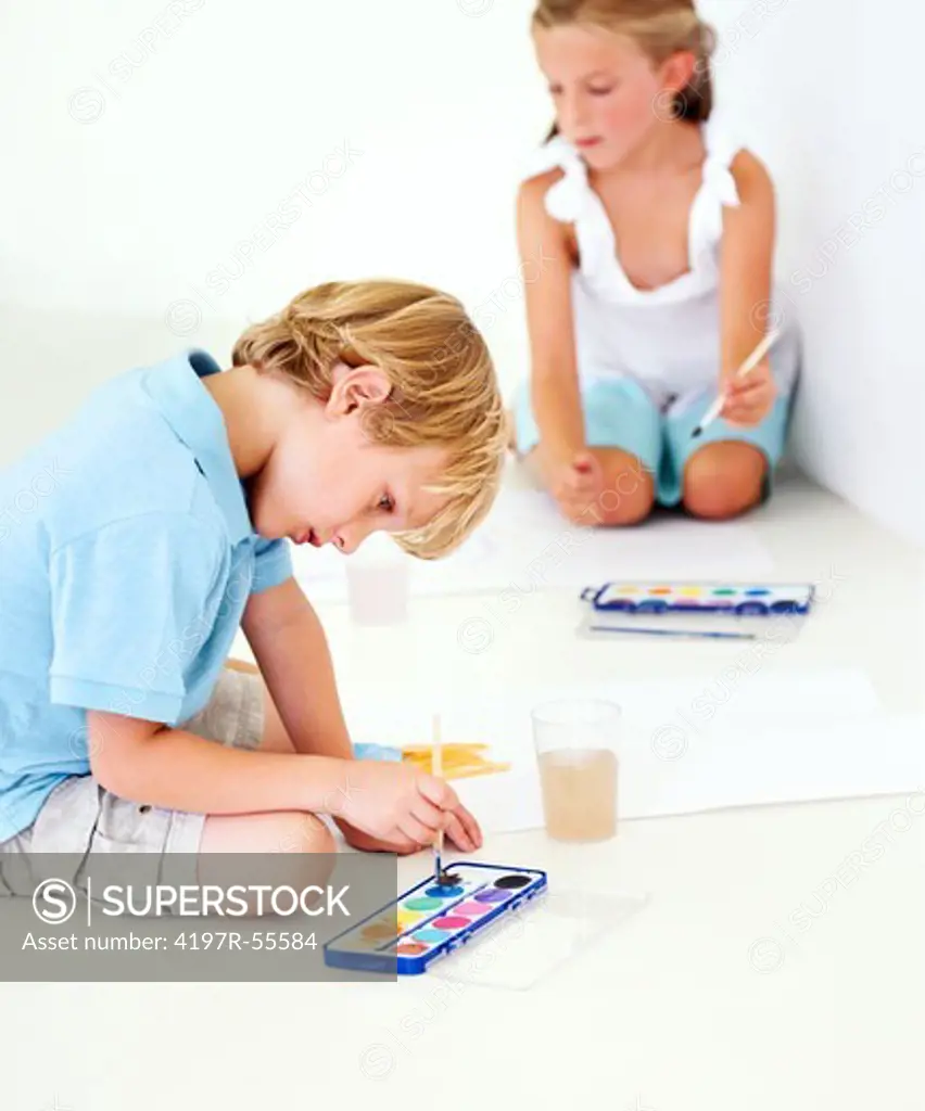 Siblings sitting on the floor painting watercolour pictures together