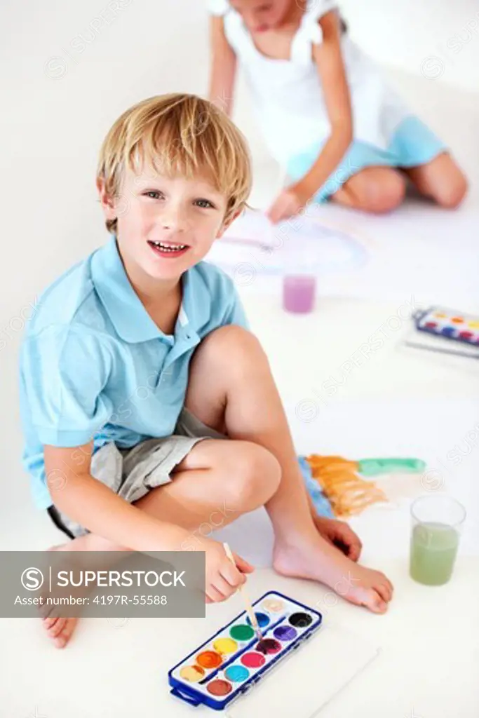 High angle portrait of a young boy painting watercolour pictures with his sister in the background
