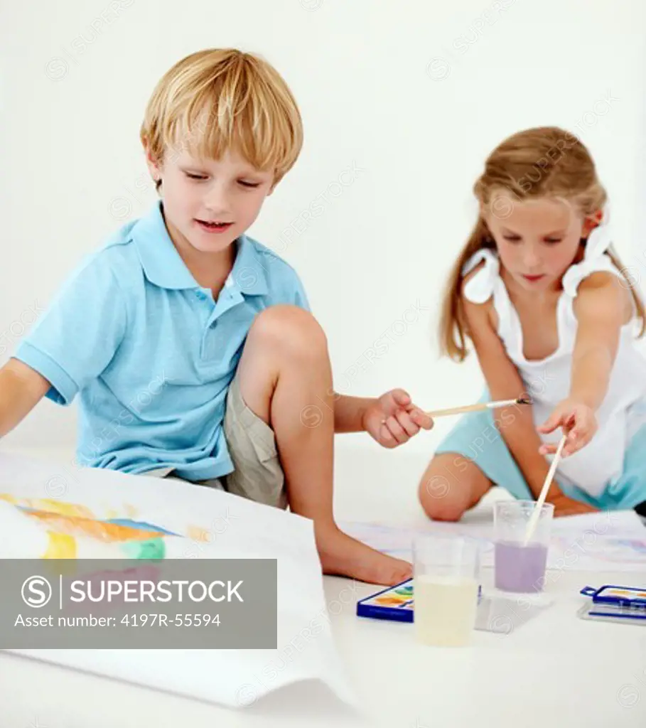 Young siblings having fun together painting pictures with watercolours