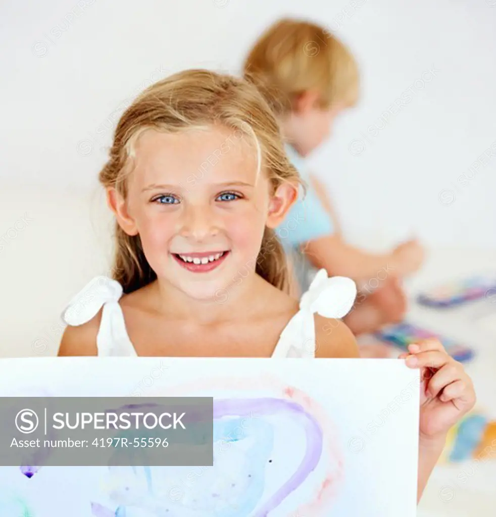 A young girl smiles broadly for the camera holding her finished painting