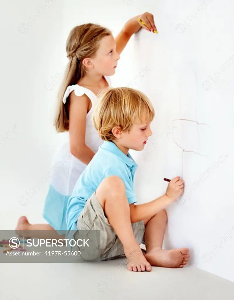 Two mischievous children drawing on the wall with crayons