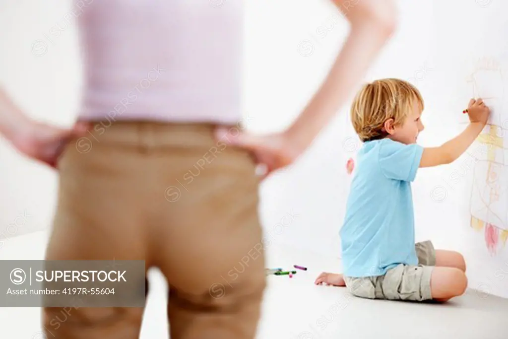 A young boy about to be scolded by his mom for drawing on the wall with crayons