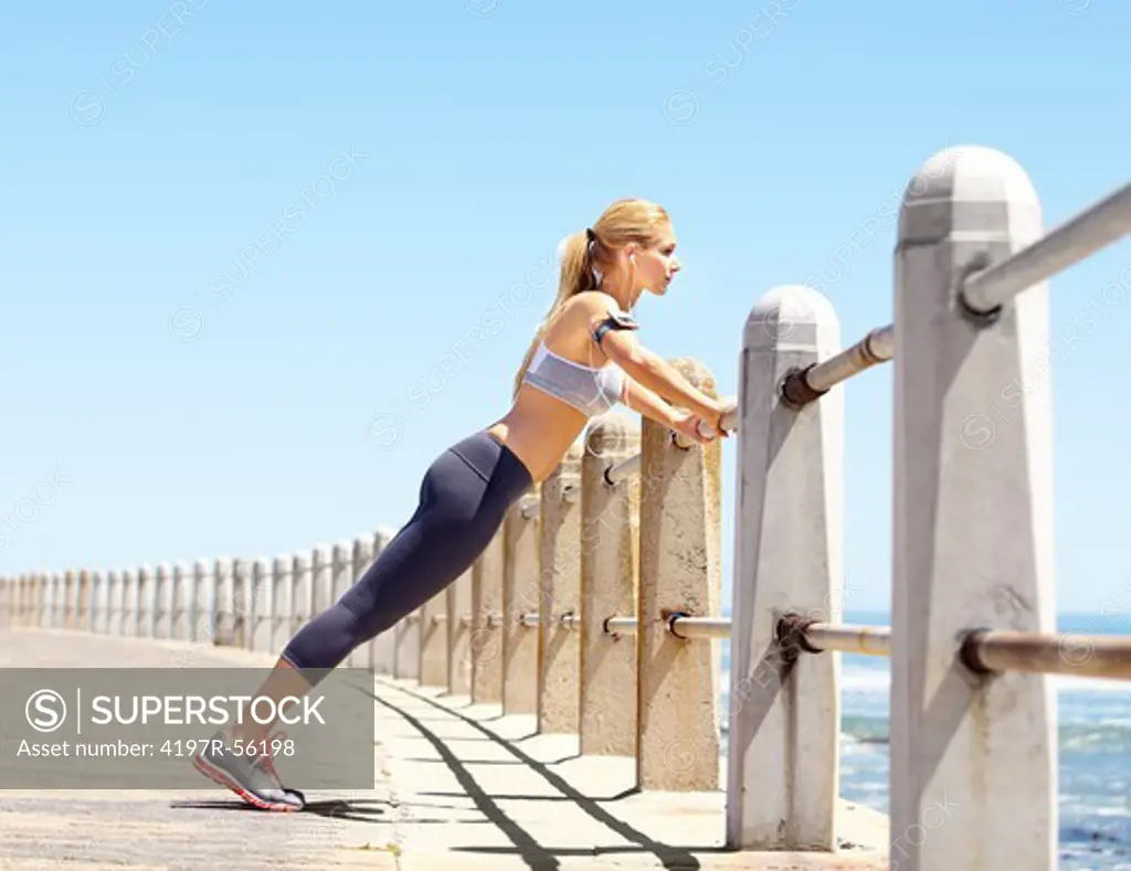 An attractive young woman using the barrier as an aid to her exercising routine