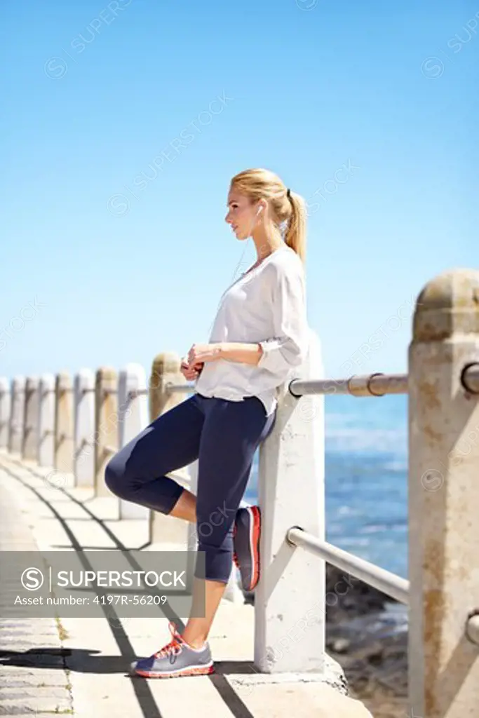 An attractive young woman leaning against the barrier listening to music through her earphones