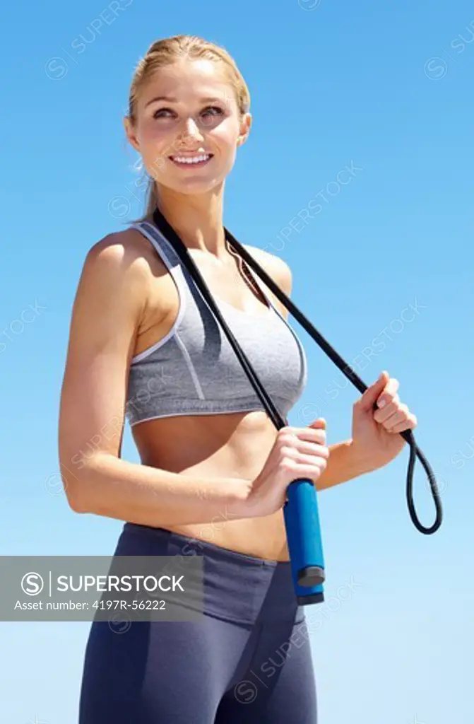 An attractive young woman standing upright and holding a skipping rope over her shoulders