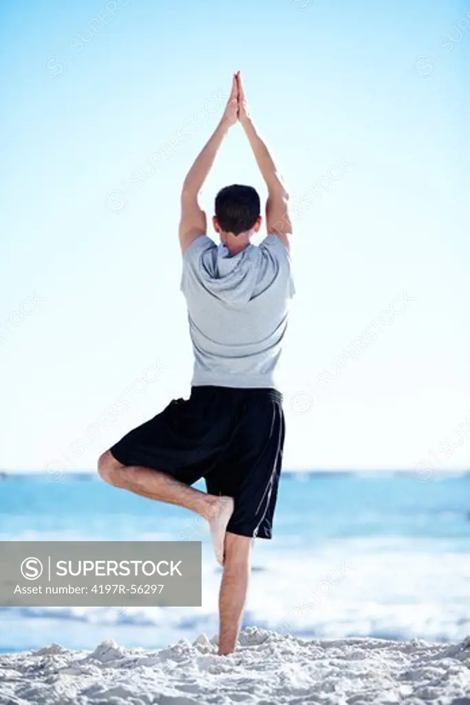 Fit young man doing yoga on the beach - rear view