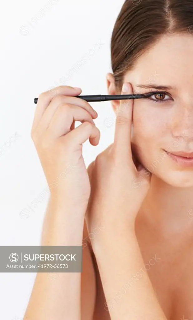 Beautiful young woman applying eyeliner while isolated on white