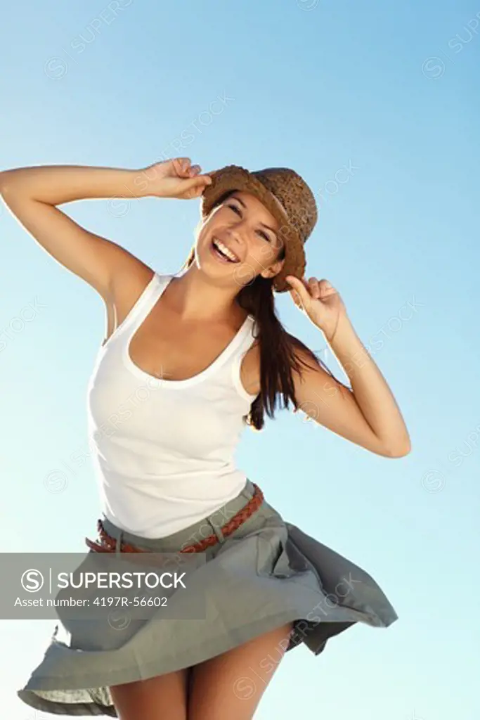 Laughing young woman isolated against a blue sky while holding her hat brim