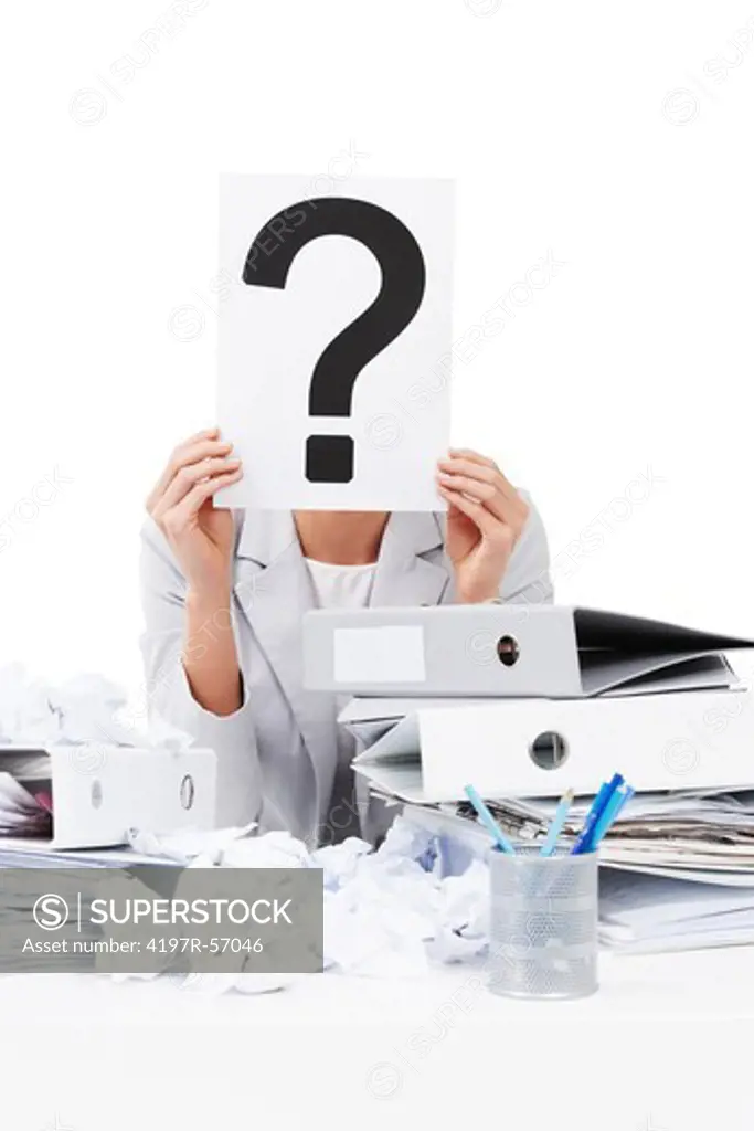A businesswoman holding up a placard with a question mark on it while sitting at her desk