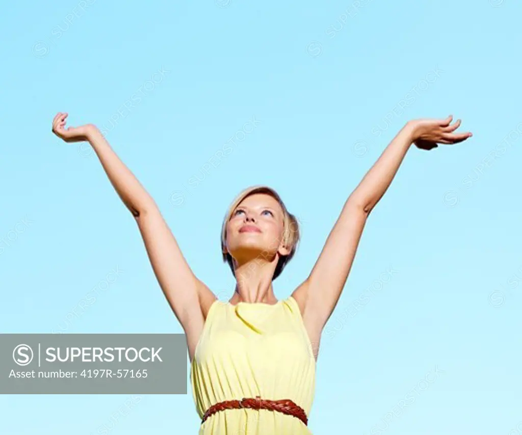 A pretty young woman standing with her arms raised with a blue sky in the background