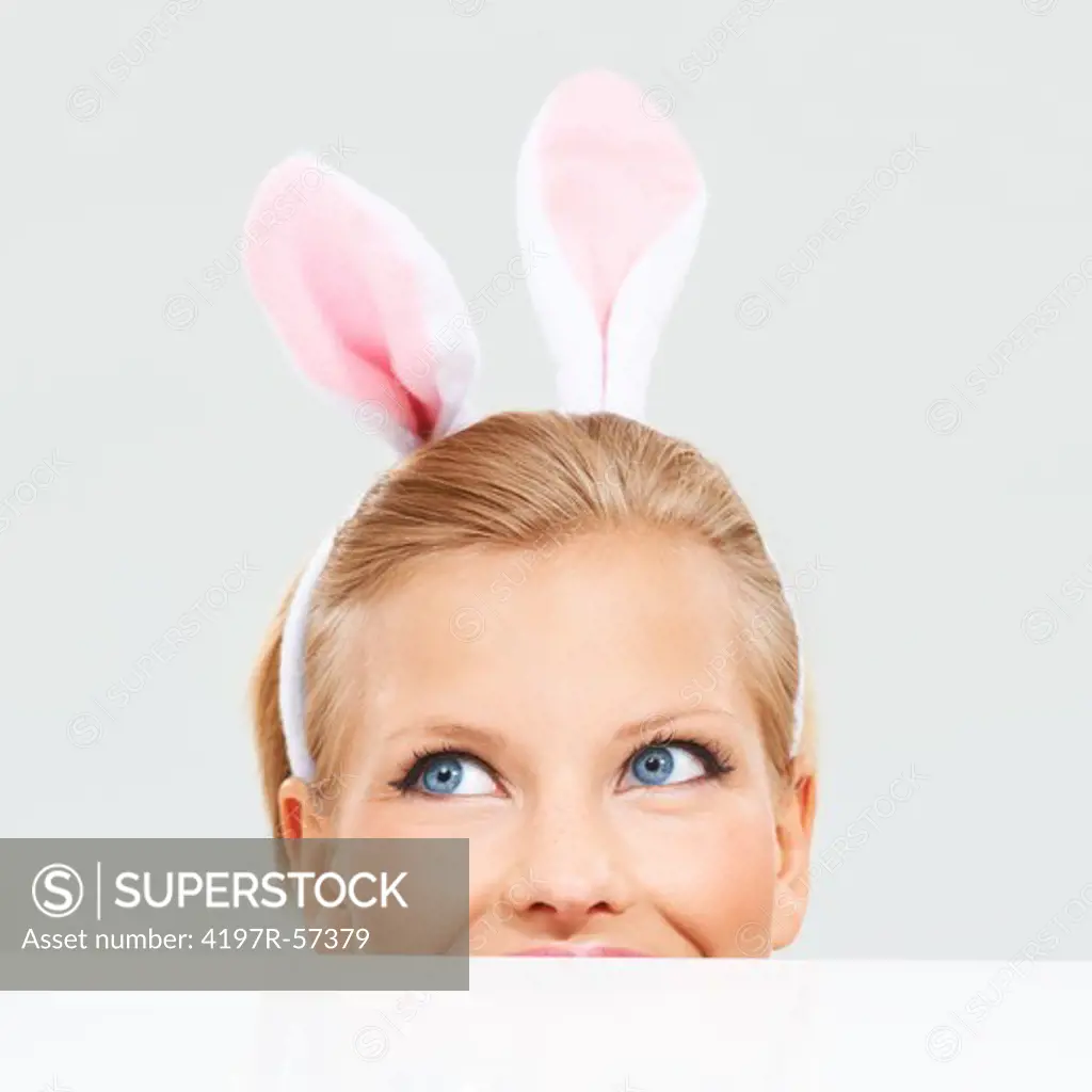 Pretty young woman wearing bunny ears and peeking over a a surface