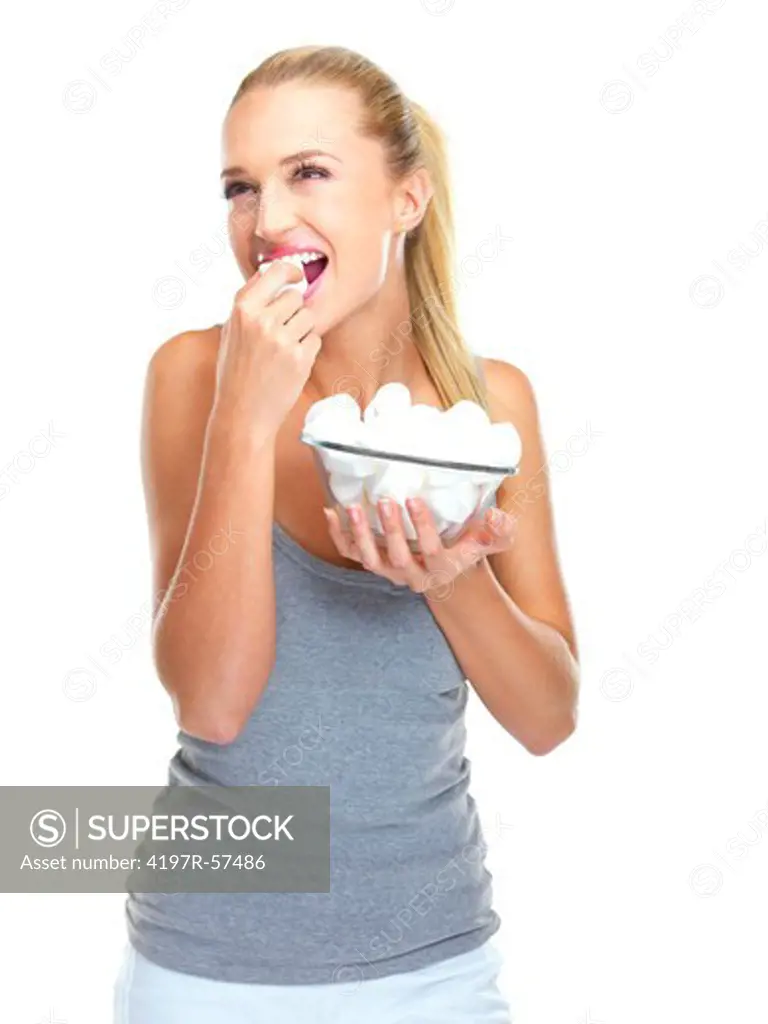 Positive young woman holding a bowl of marshmellows while eating one
