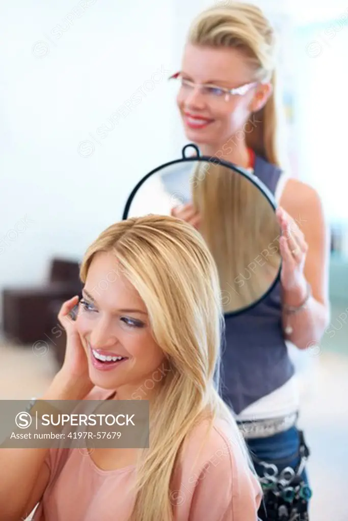 Hairstylist showing a pretty young client the back of her hair in the salon