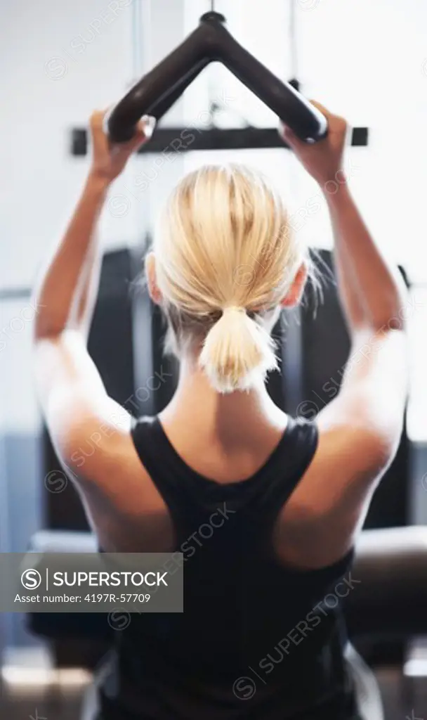 Rear view of an attractive young woman working her shoulders in the gym