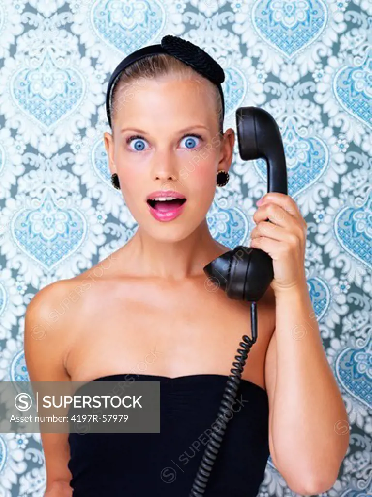 Pretty young woman on a retro telephone and receiving pleasantly surprising news