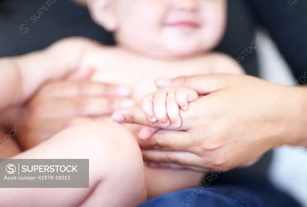 A baby boy holding his mother's hands while sitting on her lap