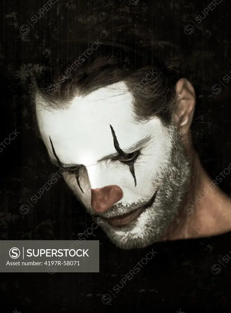 A man with clown paint on his face looking down on a black background