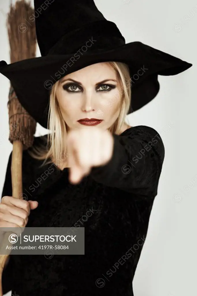 Portrait of a beautiful blonde witch with a broomstick pointing at you on a white background