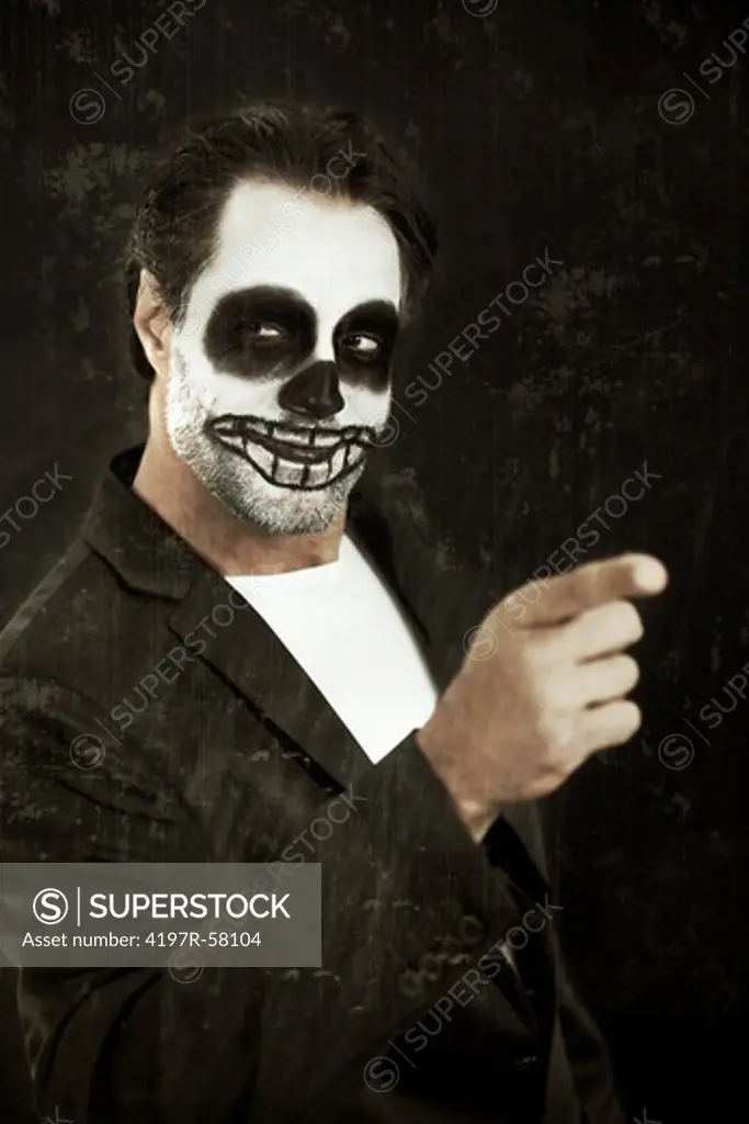 A man with his face painted like a skull for halloween pointing on a black background