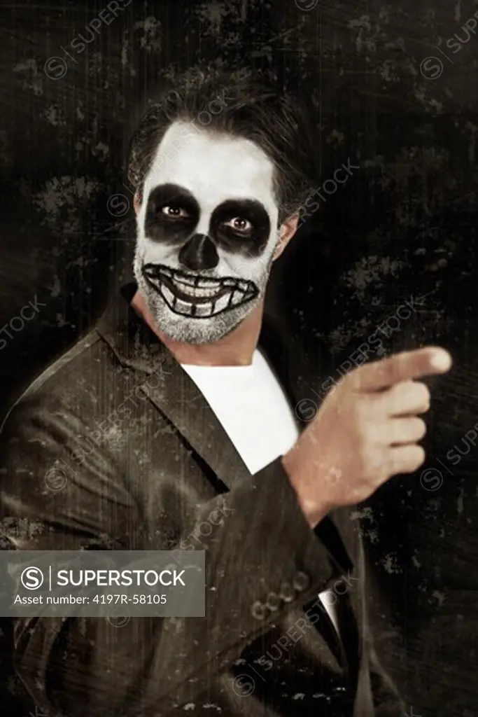 Portrait of a man with his face painted like a skull for halloween pointing his finger on a black background