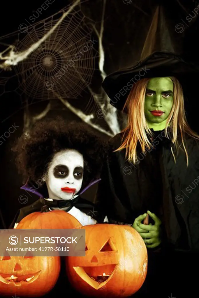 Portrait of two children dressed up for Halloween with jack-o-lanterns in front of them