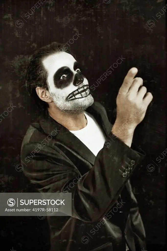 A man with his face painted like a skull for Halloween pointing on a black background